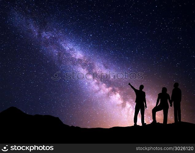 Milky Way with silhouette of a standing young man pointing finger in night starry sky and his parents. Colorful night landscape. Beautiful Universe, travel background with sky full of stars