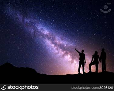Milky Way with silhouette of a standing young man pointing finger in night starry sky and his parents. Colorful night landscape. Beautiful Universe, travel background with sky full of stars