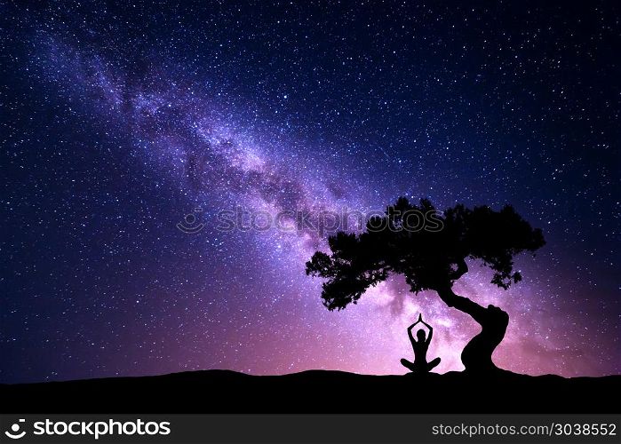 Milky Way with tree and woman practicing yoga. Milky Way with tree and silhouette of a sitting woman practicing yoga. Beautiful landscape with meditating girl under the tree against starry sky with purple milky way. Galaxy. Beautiful universe