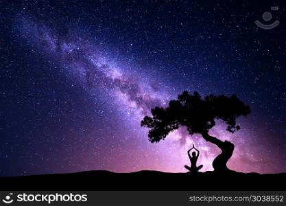 Milky Way with tree and woman practicing yoga. Milky Way with tree and silhouette of a sitting woman practicing yoga. Beautiful landscape with meditating girl under the tree against starry sky with purple milky way. Galaxy. Beautiful universe