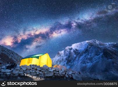Milky Way, yellow glowing tent and mountains. Amazing scene with himalayan mountains, starry sky at night in Nepal. Rocks with snowy peak and sky with stars. Night landscape with milky way. Space