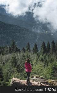 Millenial girl on a rock admiring the Hornisgrinde mountains covered by fir forest and clouds, in the Black Forest, Germany. Travel destination.