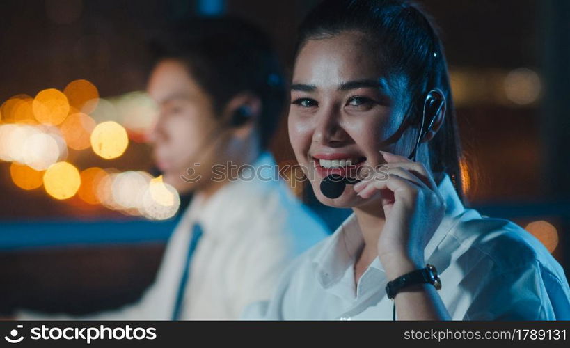 Millennial Asia young call center team or customer support service executive using computer and microphone headset working technical support in late night office. Telemarketing or sales job concept.