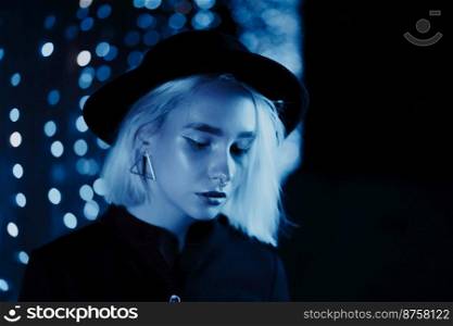 Millennial enigmatic pretty girl blond hairstyle near glowing neon wall at night. Blue hair, hipster hat, nose piercing. Mysterious woman. High quality photo. Millennial enigmatic pretty girl blond hairstyle near blue glowing neon wall at night. Hair, hipster hat, nose piercing. Mysterious woman