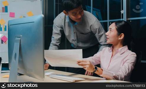 Millennial group of young Asia businessman and businesswoman in small modern night office. Indian male boss supervisor teaching intern or new employee korean girl helping with difficult assignment.
