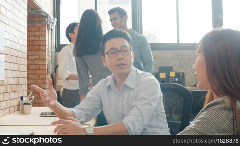 Millennial group of young Asia businessman and businesswoman in small modern urban office. Japanese male boss supervisor teaching intern or new employee korean girl helping with difficult assignment.