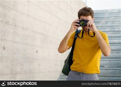 Millennial man taking photographs with a SLR camera outdoors. Millennial man taking photographs with a SLR camera