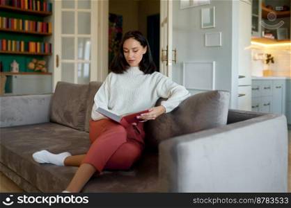 Millennial woman reading book sitting in cozy sofa at home. Enjoyment of lazy morning, having relax on weekend. Millennial woman reading book sitting in cozy sofa at home