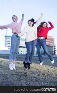 Millennial women jumping outdoor - Happy girls friends having fun in urban city park - Generation z, youth, young people lifestyle concept - Focus on right female body