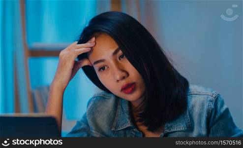 Millennial young Chinese businesswoman working late night stress out with project research problem on laptop in living room at modern home. Asia people occupational burnout syndrome concept.