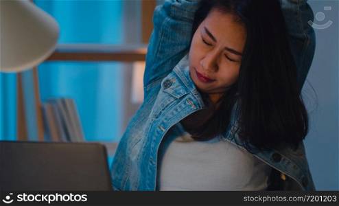 Millennial young Chinese businesswoman working late night stretching on her chair, looking in laptop computer in living room at modern home. Asia people occupational burnout syndrome concept.