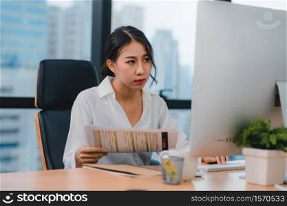 Millennial young Chinese businesswoman working stress out with project research problem on computer desktop in meeting room at small modern office. Asia people occupational burnout syndrome concept.