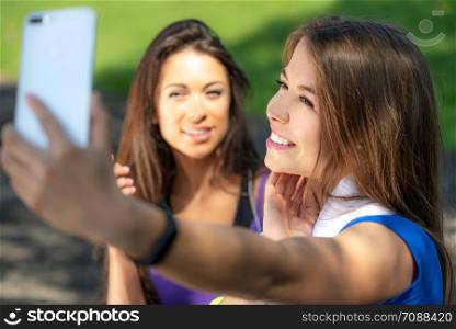 Millennials lifestyle concept - two sports girls taking a selfie and smiling after outdoors training on a sunny day.