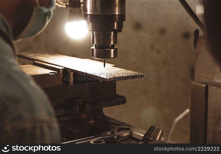 Milling machine working near worker with a protective mask. Tool for cut metal workpiece. Vertical milling machine with cemented carbide milling cutter. Steel manufacturing industry. Milling process.