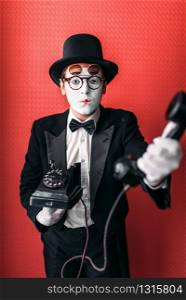 Mime theater actor performing with old telephone. Comedy pantomime artist in suit, gloves and hat. Mime theater actor performing with old telephone