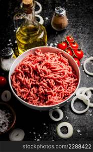 Minced meat in a bowl with onion rings, tomatoes and spices. On a black background. High quality photo. Minced meat in a bowl with onion rings, tomatoes and spices.
