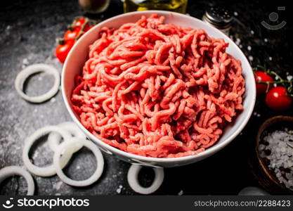 Minced meat in a bowl with onion rings, tomatoes and spices. On a black background. High quality photo. Minced meat in a bowl with onion rings, tomatoes and spices.