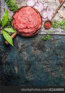 Minced meat in frying pan with wooden cooking spoon and fresh flavoring on rustic background, top view, place for text.
