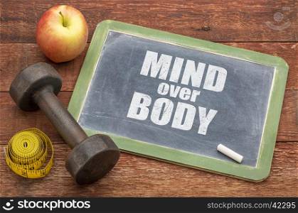 mind over body concept - slate blackboard sign against weathered red painted barn wood with a dumbbell, apple and tape measure