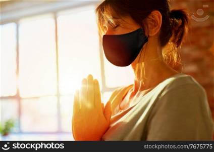 mindfulness, epidemic and people concept - close up of yogi woman wearing face protective black mask for protection from virus disease meditating at yoga studio. woman in black mask meditating at yoga studio
