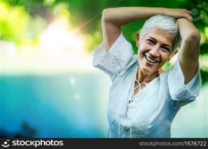 Mindfulness, portrait of a smiling beautiful senior woman by the water, enjoying nature. Beautiful smiling senior woman by the water