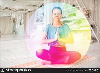mindfulness, spirituality and healthy lifestyle concept - woman meditating in lotus pose at yoga studio over rainbow aura. woman meditating in lotus pose at yoga studio