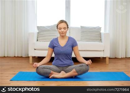 mindfulness, spirituality and healthy lifestyle concept - woman meditating in lotus pose at home. woman meditating in lotus pose at home