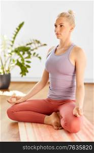 mindfulness, spirituality and yoga concept - young woman meditating in lotus pose at home. woman meditating in lotus yoga pose at home