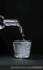 Mineral water is poured into a glass, close-up, dark background with copy space, selective focus.