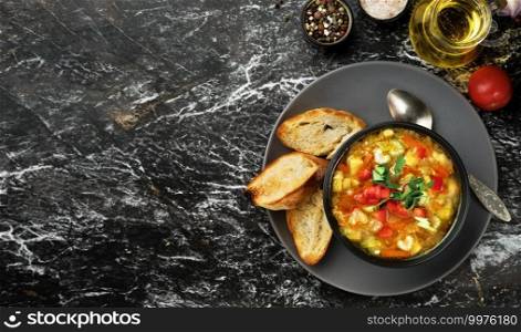 Minestrone soup in a black dish on a dark table, top view. Italian soup with seasonal vegetables. Delicious vegetarian food concept. Flat lay with copy space for text