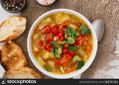 Minestrone soup in a white dish on burlap napkins, top view. Italian soup with seasonal vegetables, delicious healthy vegetarian food concept. Food diet idea. Flat lay