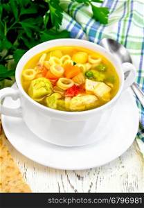 Minestrone soup with meat, celery, tomatoes, zucchini and cabbage, green peas, carrots and pasta in a bowl, towel, bread on the background light wooden boards