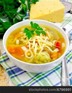 Minestrone soup with meat, celery, tomatoes, zucchini and cabbage, green peas, carrots and pasta, sprinkled grated cheese in a bowl on a towel, bread on the background light wooden boards