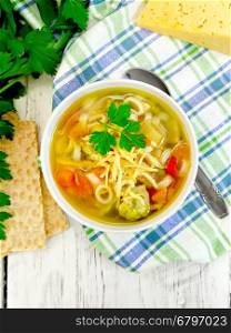 Minestrone soup with meat, celery, tomatoes, zucchini and cabbage, green peas, carrots and pasta, sprinkled grated cheese in a bowl on a napkin, bread on the background of wooden boards on top