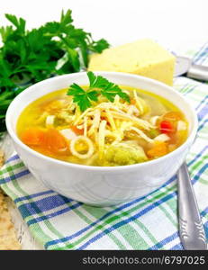 Minestrone soup with meat, celery, tomatoes, zucchini and cabbage, green peas, carrots and pasta, sprinkled grated cheese in a bowl on a napkin, bread on a wooden boards background