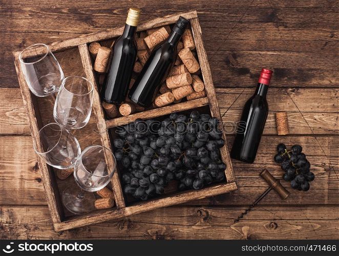 Mini bottles of red wine and empty glasses with dark grapes with corks and opener inside vintage wooden box on grunge wooden background.