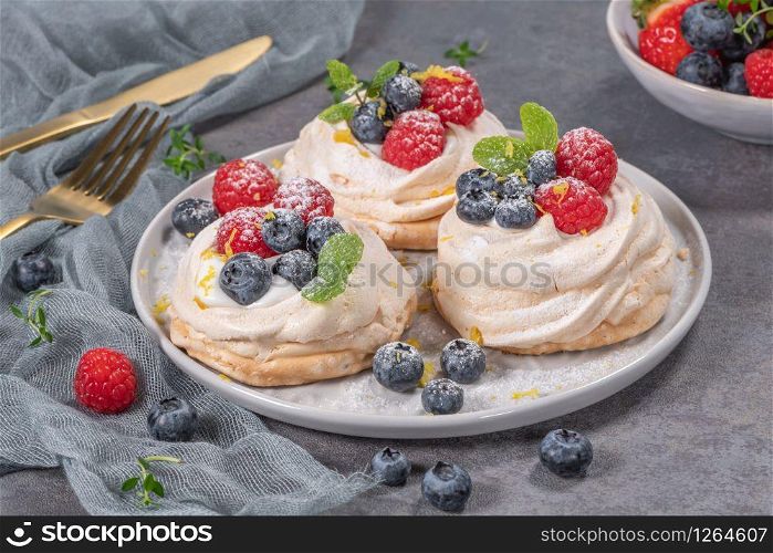 Mini pavlova meringue cakes with fresh raspberries and blueberries with mint leaves.