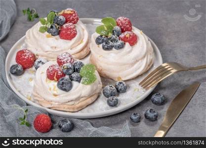 Mini pavlova meringue cakes with fresh raspberries and blueberries with mint leaves.