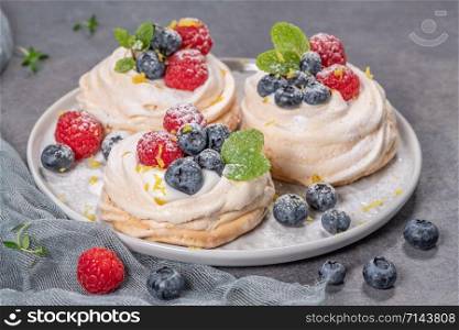 Mini pavlova meringue cakes with fresh raspberries and blueberries with mint leaves