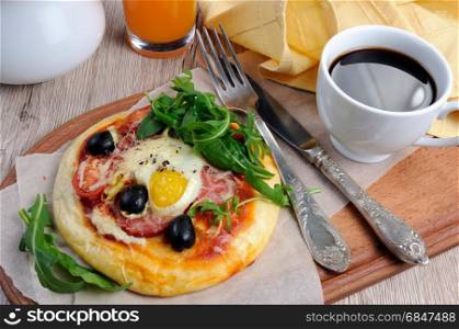 Mini pizza with sausage and egg and arugula, a cup of coffee for breakfast. Mini pizza for breakfast