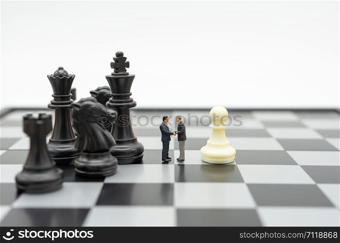 Miniature 2 people businessmen Shake hands standing on a chessboard with a chess piece on the back Negotiating in business. as background business concept and strategy concept with copy space.