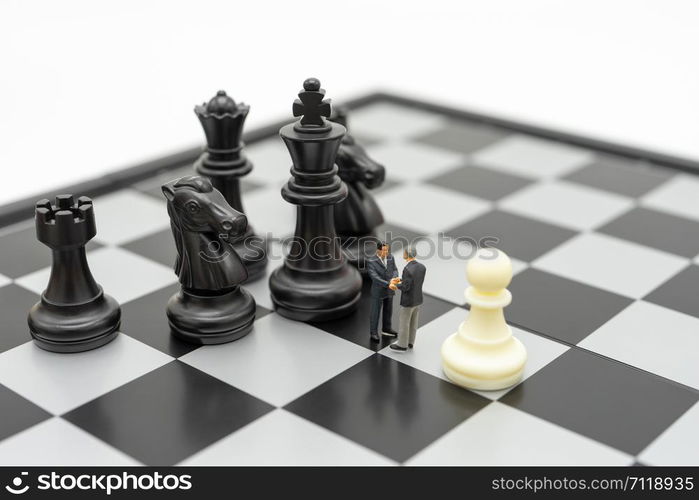 Miniature 2 people businessmen Shake hands standing on a chessboard with a chess piece on the back Negotiating in business. as background business concept and strategy concept with copy space.