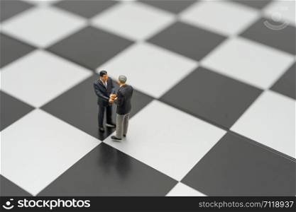 Miniature 2 people businessmen Shake hands standing on a chessboard with a chess piece on the back Negotiating in business. as background business concept and strategy concept with copy space.