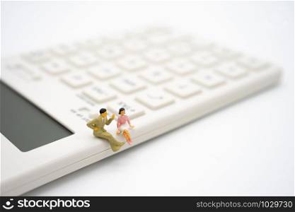 Miniature 2 people sitting on white calculator using as background business concept and teamwork concept with copy space and white space.