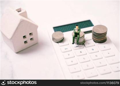 Miniature business people figure sitting on stack of coins on calculator with house, financial and real estate concept