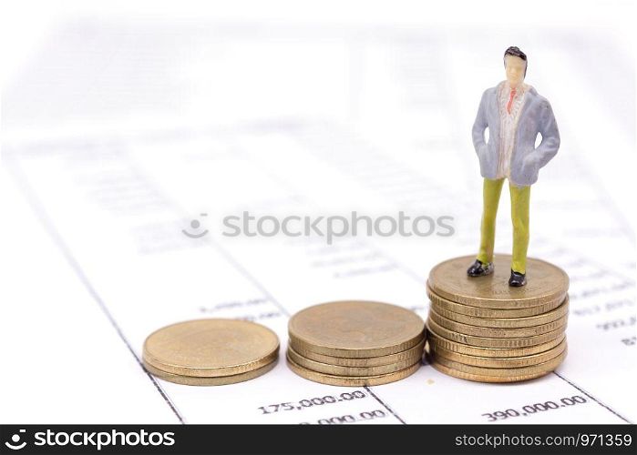 Miniature businessman and stack coins on statement