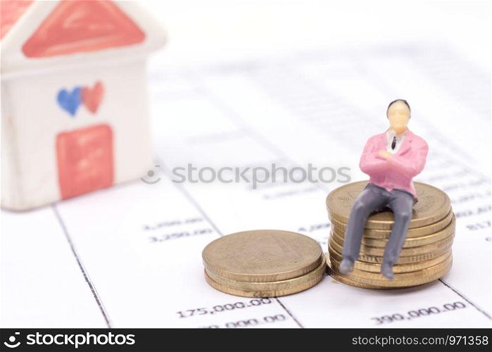 Miniature businessman and stack coins on statement and the house behind. saving and loan concept.