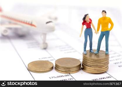 Miniature couple people and stack coins on statement and the airplane behind. saving and loan concept.