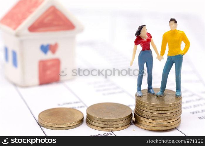 Miniature couple people and stack coins on statement and the house behind. saving and loan concept.
