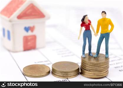 Miniature couple people and stack coins on statement and the house behind. saving and loan concept.